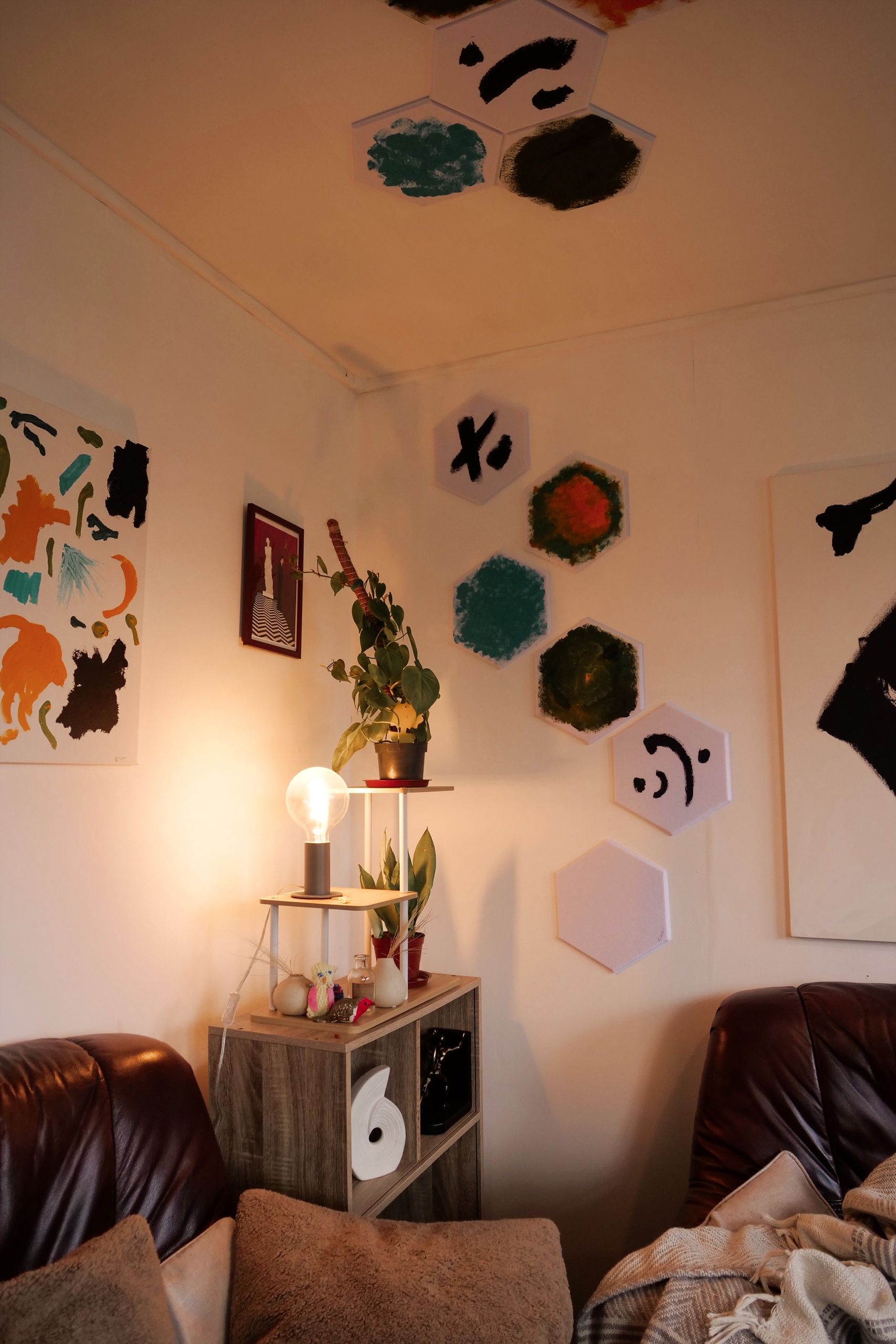 A warm and cozy living room featuring modern wall art, a small shelf with a plant, and soft lighting creating a relaxing atmosphere.