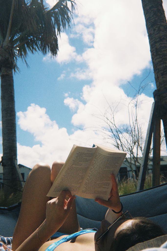 Woman enjoying a book while relaxing in a hammock under palm trees on a sunny day.